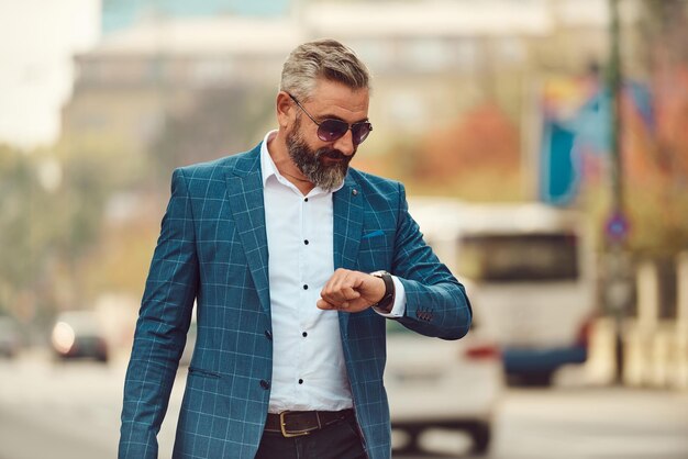 business, punctuality and people concept - senior businessman checking time on wristwatch or smart watch on his hand in city.