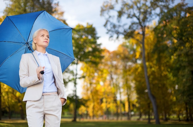 business, season, weather and people and concept - young smiling businesswoman with umbrella over autumn natural background