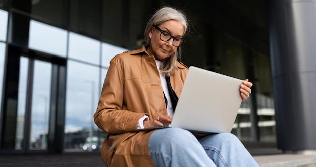 Business senior woman with laptop working online on steps of office business center