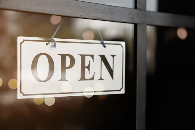 A business sign that says open on cafe or restaurant hang on door at entrance.