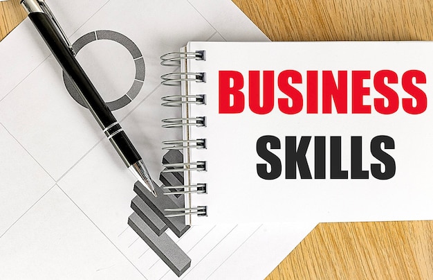 BUSINESS SKILLS text on notebook with chart on wooden background