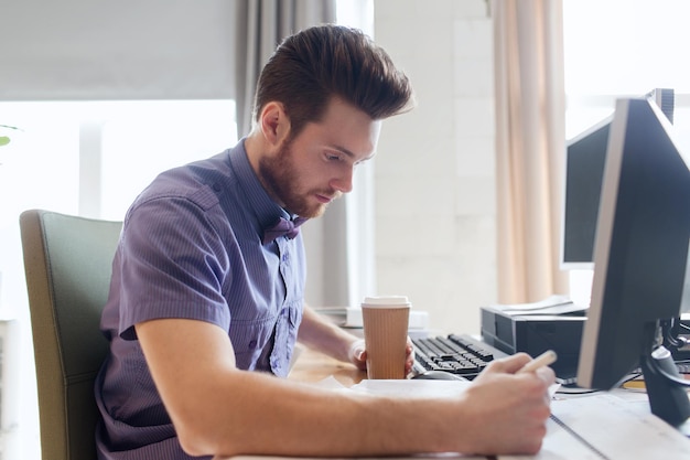 business, startup and people concept - businessman or creative male office worker drinking coffee and writing