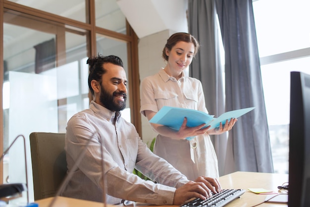 business, startup and people concept - happy creative team with computer and folder in office