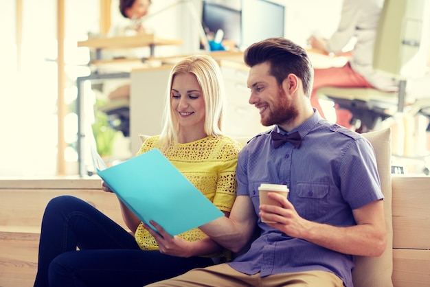 business, startup and people concept - happy man and woman with folder drinking coffee in office