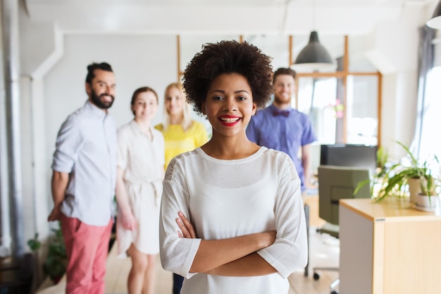 business, startup, people and teamwork concept - happy young woman over creative team in office