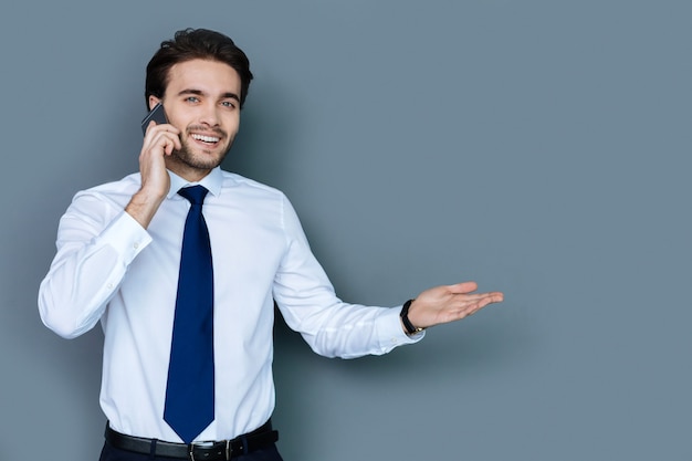 Business talk. Joyful smart positive businessman smiling and having a phone conversation while discussing business issues