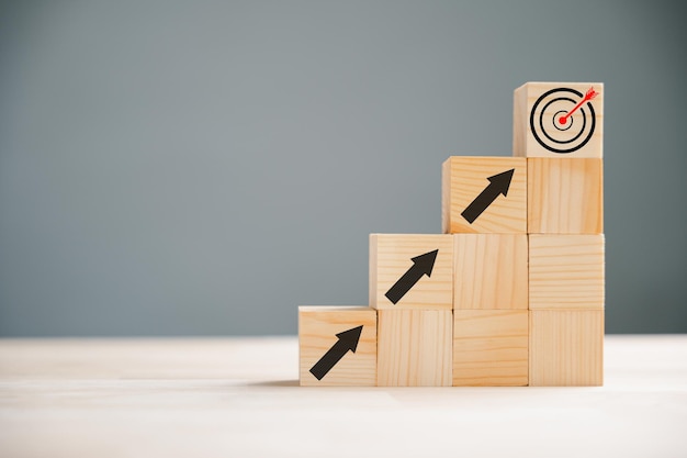 Business and target concept depicted by a hand positioning a print screen dart and wooden cube on upward arrows Symbolizing success development and financial growth White background