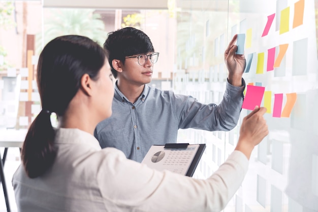 Business teamwork in meeting and adhesive stick note on mirror board discussting with team in office room for collecting some idea brainstorming plan.