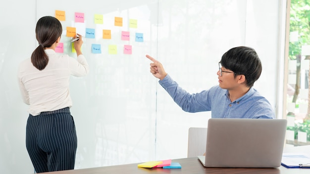 Business teamwork in meeting and adhesive stick note on mirror board discussting with team in office room for collecting some idea brainstorming plan.