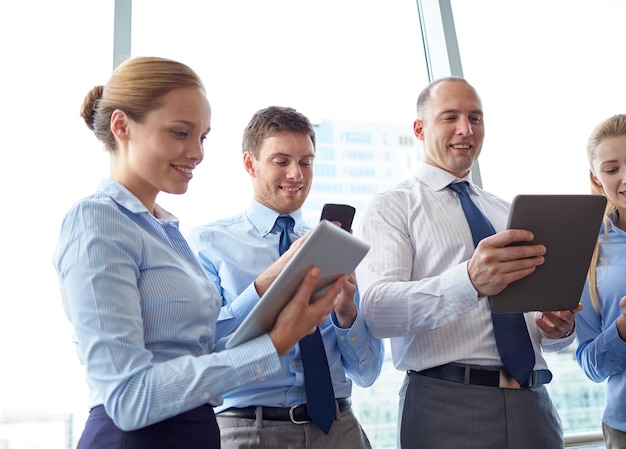 business, teamwork, people and technology concept - business team with tablet pc and smartphones in office