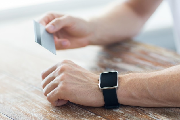 business, technology, cash free and internet people concept - close up of male hands with smart watch and credit card at office