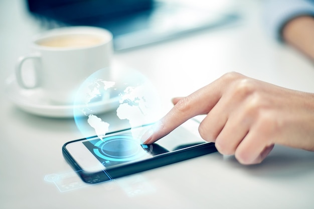 business, technology, communication, leisure and people concept - close up of woman hand with smartphone and globe hologram