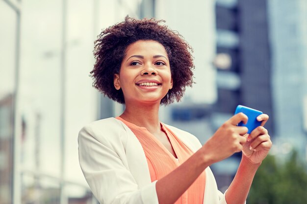 business, technology, communication and people concept - young smiling african american businesswoman with smartphone in city