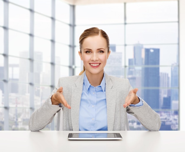 business, technology, education and people concept - smiling businesswoman sitting at table with tablet pc computer over office background