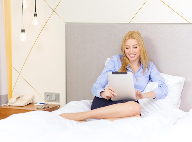 business, technology, internet and hotel concept - happy businesswoman with tablet pc computer lying in hotel in bed