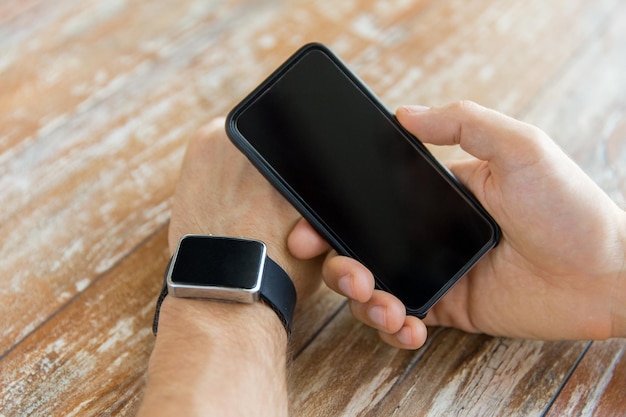 business, technology and people concept - close up of male hand holding smart phone and wearing watch at home