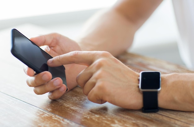 business, technology and people concept - close up of male hand holding smart phone and wearing watch at home