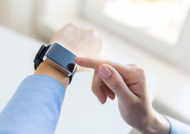 business, technology and people concept - close up of woman hands setting smart watch at office