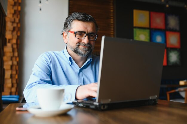 Business technology and people concept senior businessman with laptop computer drinking coffee at modern cafe