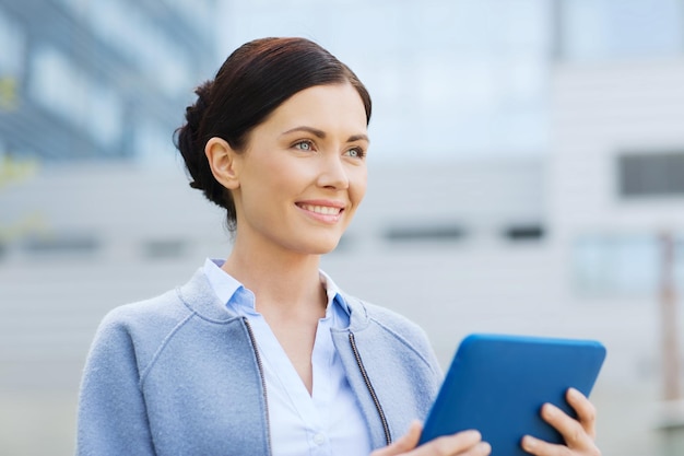 business, technology and people concept - young smiling woman with tablet pc computer over office building