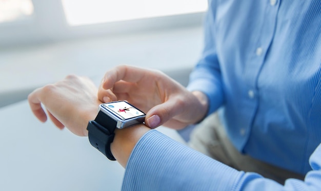 business, technology, sport and people concept - close up of woman hands setting smart watch with fitness application at office