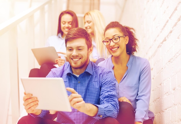 business, technology and startup concept - smiling creative team with tablet pc computer sitting on staircase