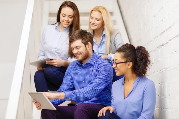 business, technology and startup concept - smiling creative team with tablet pc computer sitting on staircase