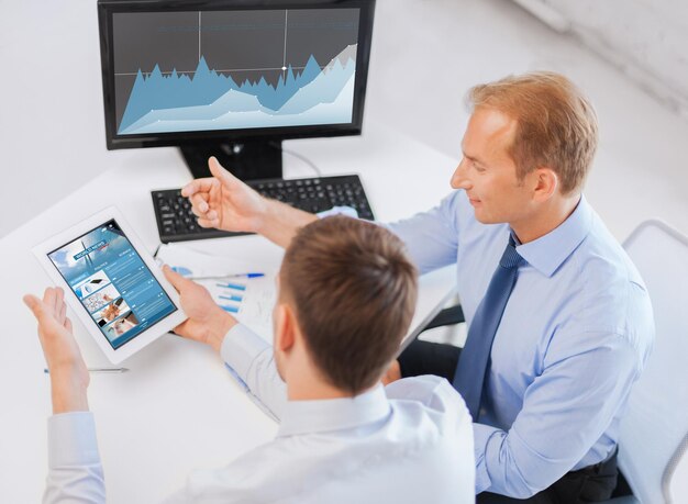 business, technology, statistics, economics and people concept - businessmen with charts on tablet pc and computer at office