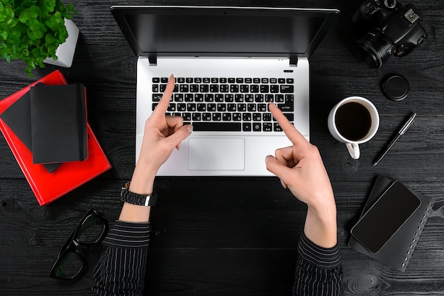 Business and technology topic: hand in a black shirt showing gesture against a black and white background laptop at the desk.