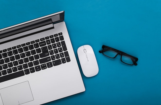 Business theme. Laptop with glasses on blue background. Top view