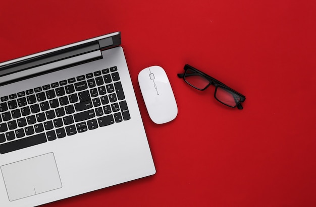 Business theme. Laptop with glasses on red background. Top view