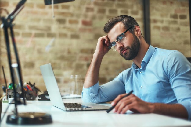 Business thoughts side view of young bearded businessman in eyeglasses and formal wear thinking