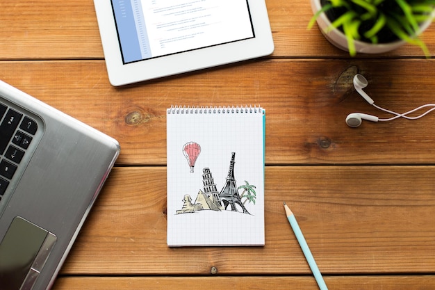 business, tourism, business and technology concept - close up of notebook with landmarks drawing, laptop and tablet pc computer on wooden table