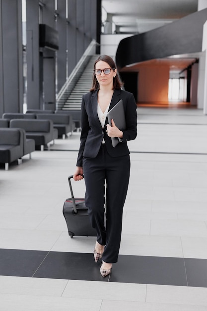 Business tourism business woman in a formal suit with a smartphone in a business center or airport with a suitcase goes on a business trip