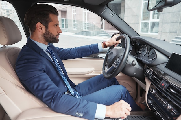 Business trip side view of confident and handsome young businessman in formal wear driving his