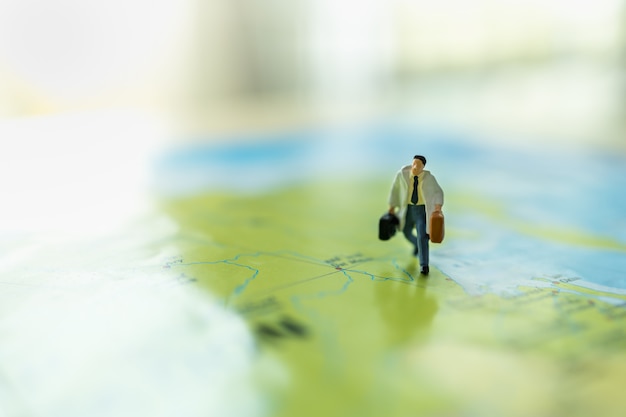 Photo business trip and travel concept. close up of businessman miniature figure with handbag suitcase running on colorful world map