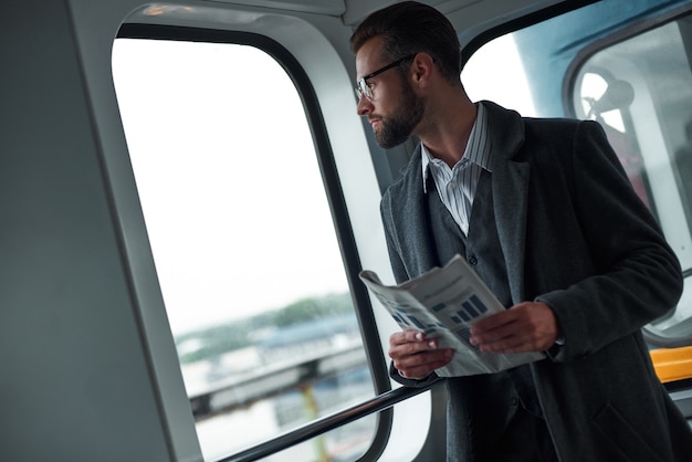 Photo business trip young businessman standing in the train holding newspaper looking out the window