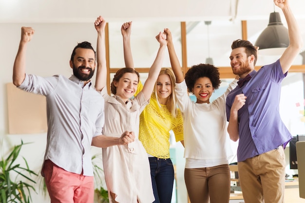 business, triumph, gesture, people and teamwork concept - happy international creative team raising hands up and celebrating victory in office