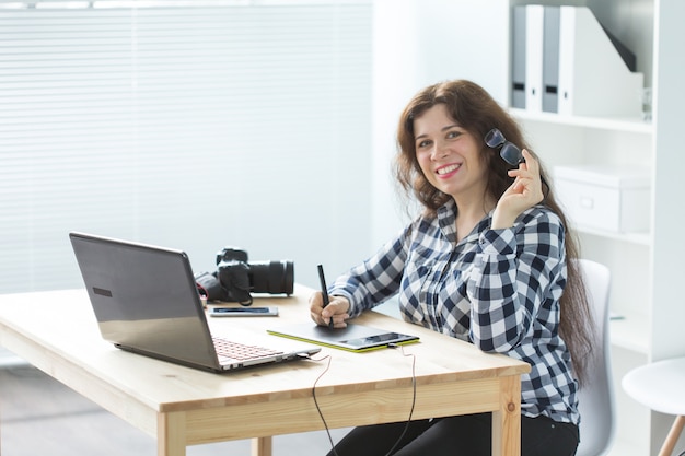 Business, web design and people concept - woman use graphic tablet in working at laptop and smiling