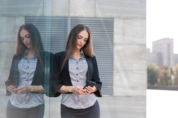 Business woman 35 years dressed stripe shirt and black jacket with long hair standing near office building outdoor use smartphone