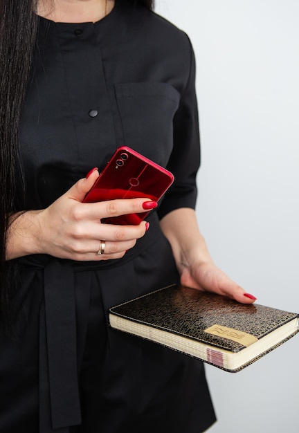 A business woman in a black uniform is standing holding a smartphone and a notebook about work in her beauty salon Concept of small business beauty salon and self care