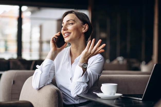 Business woman in a cafe working on laptop and using phone