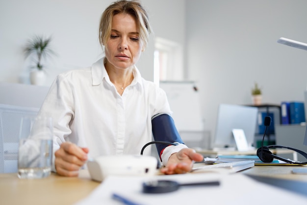 Business woman checking blood presure while sitting at workplace