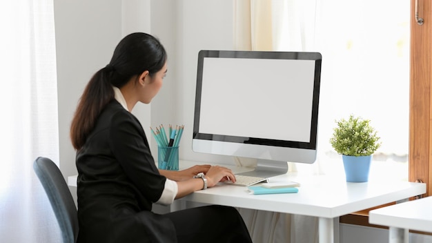 Business woman concentrating on her work on pc desktop computer in her modern minimal office room.