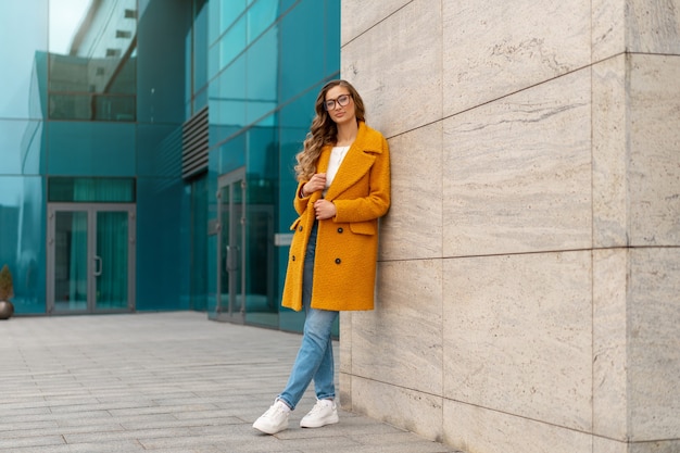 Business woman dressed yellow coat standing outdoors corporative building background Caucasian female business person eyeglasses on city street near office building with windows Stylish businesswoman