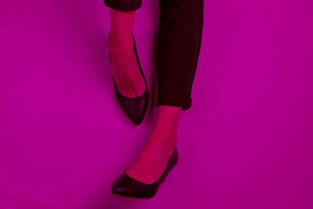 Business woman flat lay concept. Female legs dressed in trousers and classic shoes with heels in pink neon light. Top view. Beauty and fashion studio shot