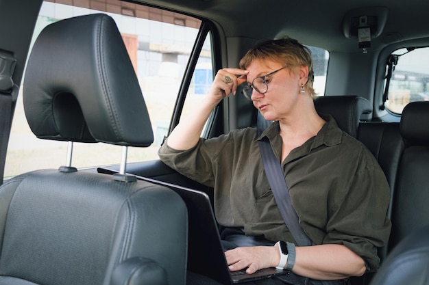 Business woman in glasses is talking on the phone while sitting in the back seat of a car