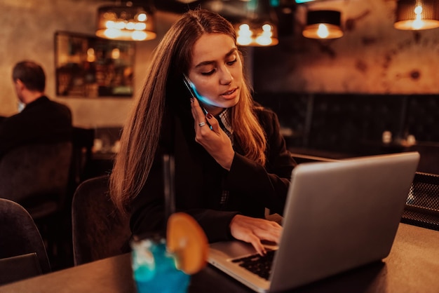 A business woman in glasses sitting in a cafe using a laptop and a smartphone for online meeting Selective focus