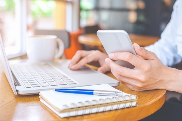 Business woman hand holding a mobile phone and working on a laptop in an office.