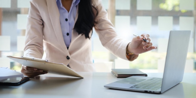 Business woman hand holding pencil and financial paperwork looking at bank savings account application on laptop computer account or saving money or insurance concept